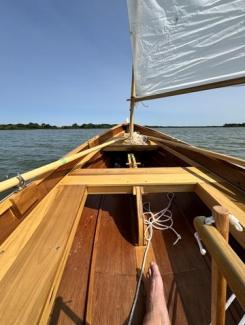 Arch Davis Penobscot 13’ Skiff, in water, sail up, looking down toward bow