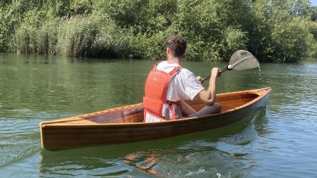 Tom paddling down a river, backdropped by trees. 