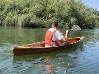 Tom paddling down a river, backdropped by trees. 