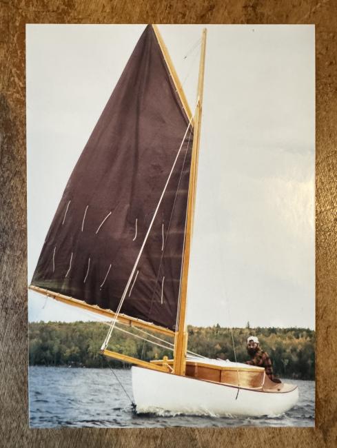 Gaff rigged wooden sailboat with trailer, undersail, port side bow view